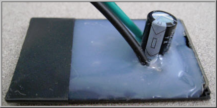poorly designed battery blank showing capacitor and two wires submerged in melted looking plastic