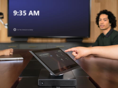 Un utente tocca una Teams Rooms console, con uno schermo sullo sfondo.