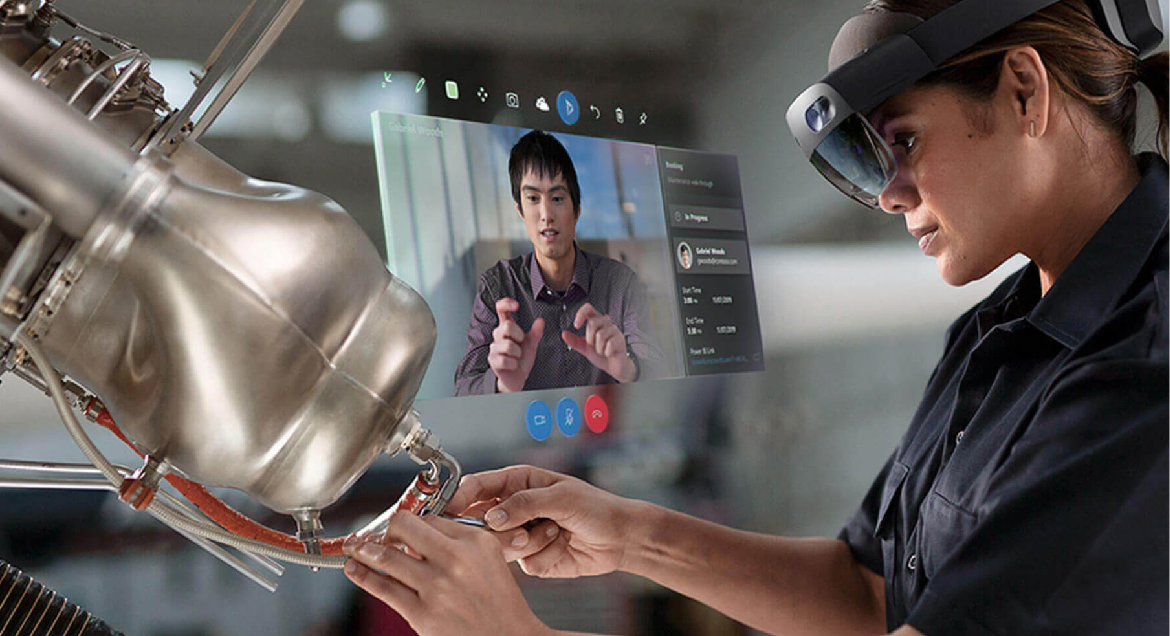 Fotografia użytkownika urządzenia HoloLens wykonującego naprawę mechaniczną podczas korzystania z aplikacji Remote Assist do komunikowania się ze współpracownikiem.
