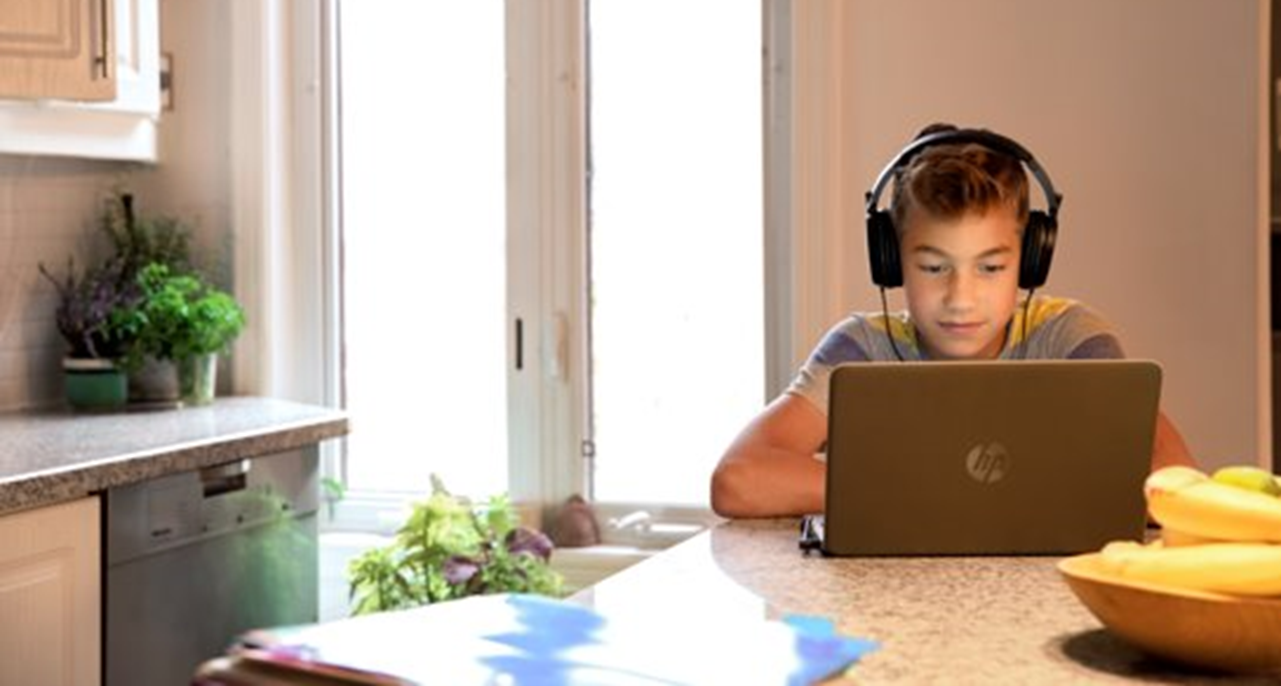Imagem de um aluno trabalhando com um computador pessoal e um headset.